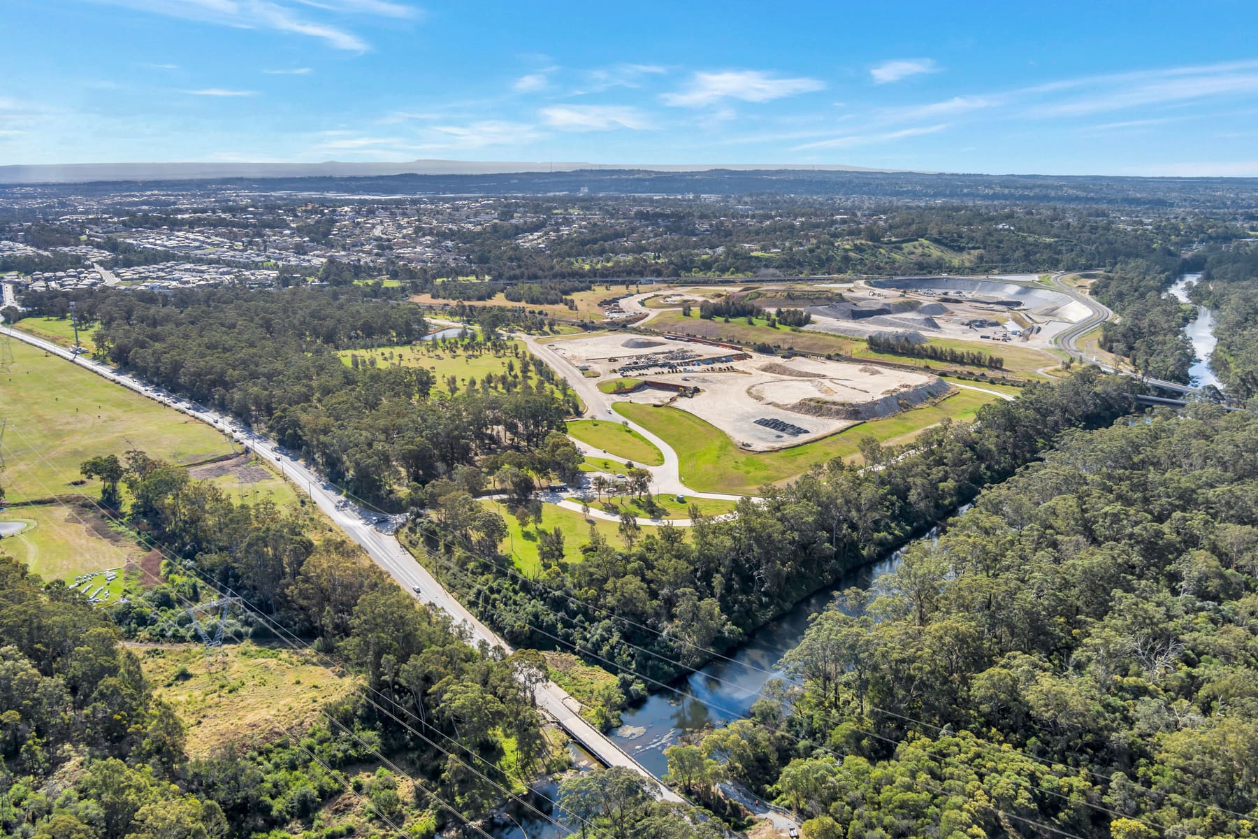 An aerial view of the Glenfield Waste Services site — benched earthworks and a working floor set among bushland, with Cambridge Avenue and the river running past.