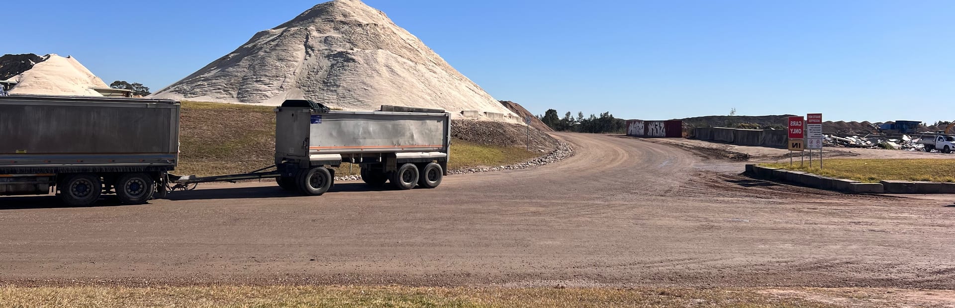A tipper and dog trailer on the site road at Glenfield Waste Services, with a stockpile rising behind them.