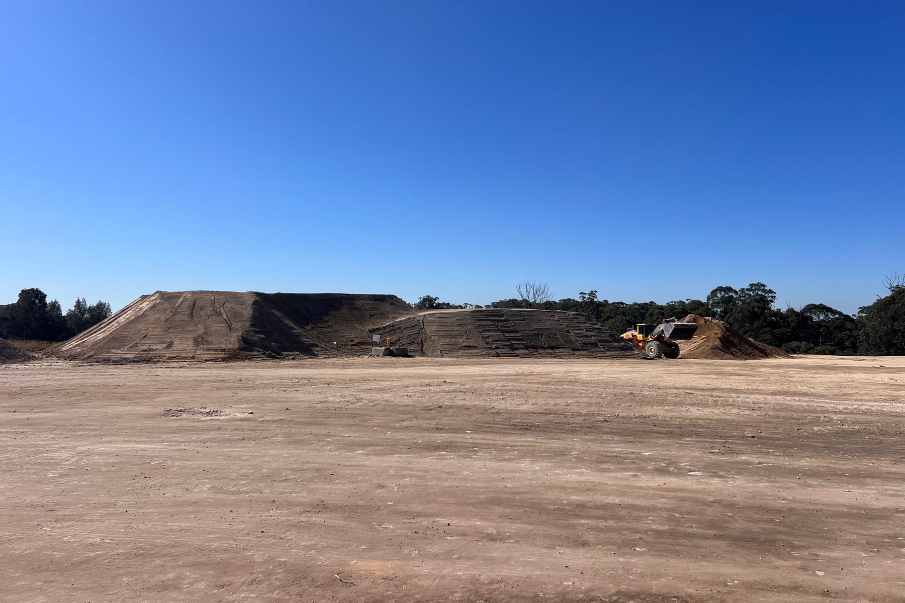 The working floor at Glenfield Waste Services, with the benched landform behind it and a loader at a soil stockpile.
