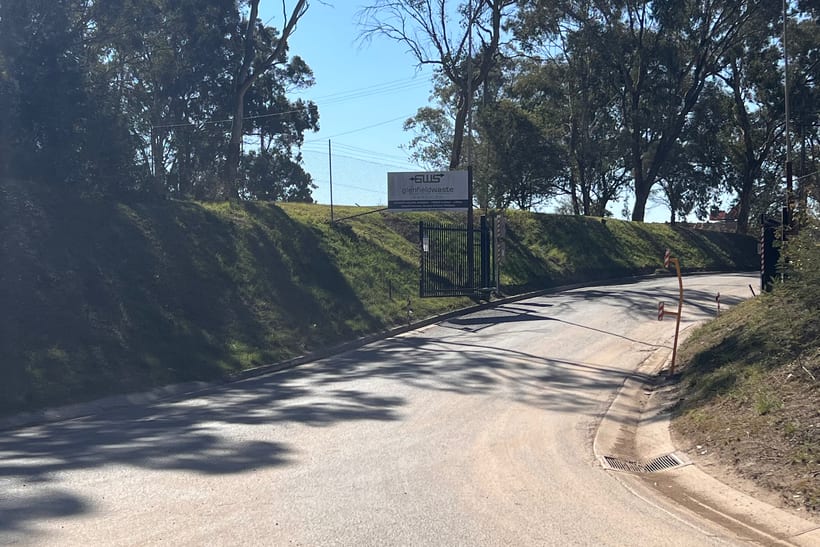 The approach road to Glenfield Waste Services, with the site sign and the boom gate ahead.